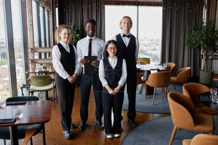 Téléchargez les photos : Portrait complet du personnel du restaurant avec des serveurs portant des uniformes classiques en noir et blanc debout dans la salle à manger et regardant la caméra - en image libre de droit