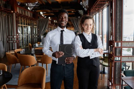 Téléchargez les photos : Portrait taille haute de deux jeunes gens comme personnel de restaurant de luxe portant des uniformes noirs et blancs classiques souriant à la caméra, espace de copie - en image libre de droit