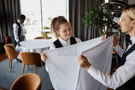 Photo for Portrait of smiling young people folding fresh tablecloths while preparing luxury restaurant for grand opening, copy space - Royalty Free Image