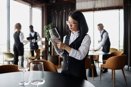 Téléchargez les photos : Portrait de vue latérale de la jeune femme asiatique comme serveur polissage des lunettes dans un restaurant de luxe, espace de copie - en image libre de droit