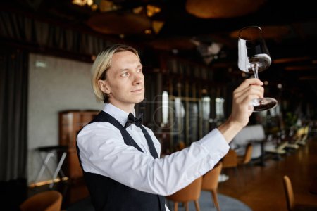 Tailliertes Porträt eines eleganten jungen Kellners mit Kristallweinglas im Restaurantinneren, Kopierraum