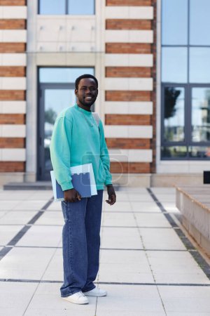 Téléchargez les photos : Vertical pleine longueur portrait du jeune homme noir comme étudiant à l'extérieur sur le campus de l'université souriant à la caméra - en image libre de droit
