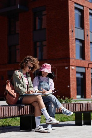 Foto de Retrato completo de dos jóvenes estudiantes que trabajan juntas en proyectos al aire libre en el campus universitario - Imagen libre de derechos