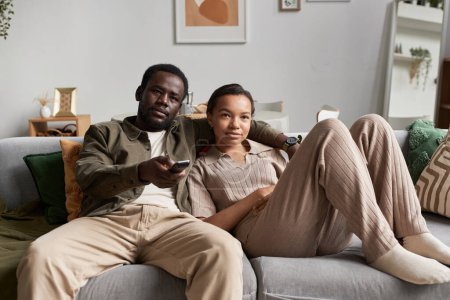 Téléchargez les photos : Vue de face portrait de jeune couple afro-américain regardant la télévision ensemble et tenant des canaux de commutation à distance - en image libre de droit