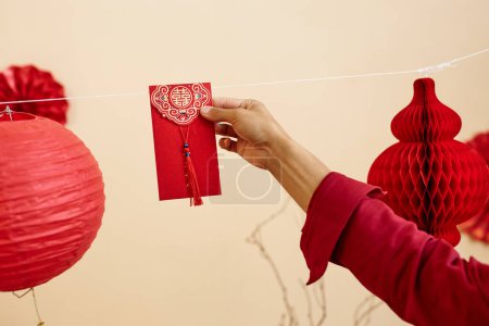 Foto de Mínimo primer plano de la mano femenina colgando sobre rojo en la cuerda para la buena fortuna como tradición de Año Nuevo chino, espacio de copia - Imagen libre de derechos