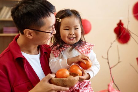 Foto de Cintura hacia arriba retrato de la muchacha asiática feliz sosteniendo naranjas para la buena suerte celebrando año nuevo chino con el padre en casa, espacio de copia - Imagen libre de derechos