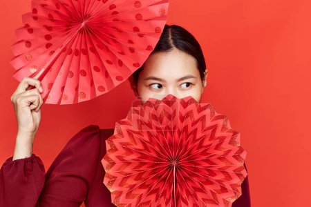 Foto de Retrato de una joven asiática bailando con abanicos de papel sobre fondo rojo en estudio - Imagen libre de derechos