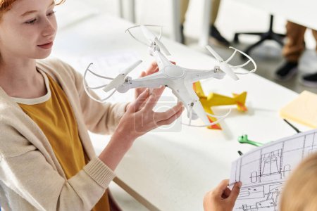 Schoolgirl examining quadcopter she assembled with classmate