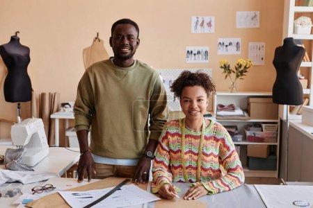 Téléchargez les photos : Deux jeunes créateurs de mode afro-américains regardant la caméra avec des sourires tandis que le tailleur féminin contouring motifs de papier à coudre - en image libre de droit