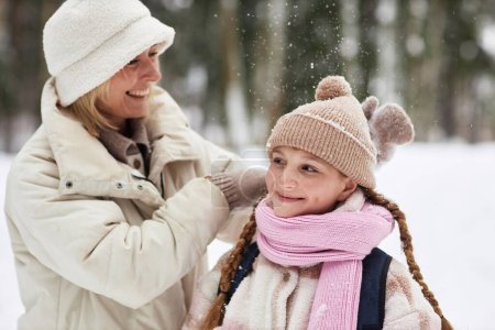 Young woman in warm winterwear playing with her pre-teen daughter in forest on winter weekend and enjoying being together