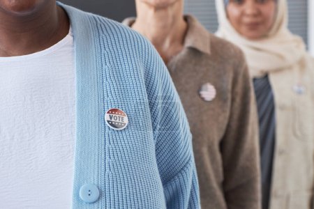 Photo for Close-up of young African American woman in blue cardigan with vote badge on chest standing in front of other voters during elections - Royalty Free Image