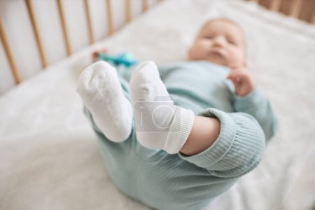 Closeup of cute baby feet with little boy laying in crib and playing happily, copy space