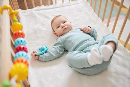 Photo for High angle portrait of cute baby boy laying in bassinet and looking at camera playing with rattle toy, copy space - Royalty Free Image