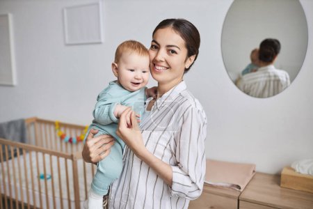 Photo for Waist up portrait of happy young mother holding baby boy in cozy room and smiling at camera, copy space - Royalty Free Image