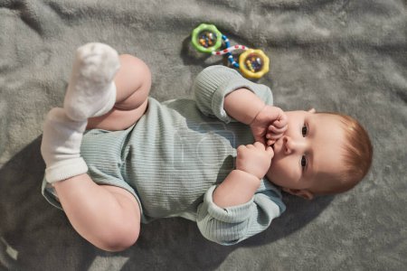 Photo for Top view portrait of cute baby boy with blue eyes laying on soft grey blanket and wiggling his legs - Royalty Free Image