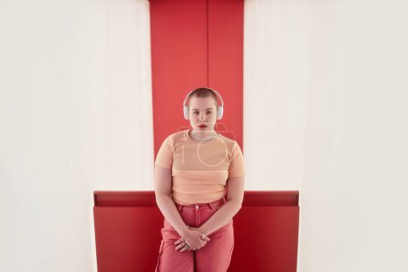 Cintura gráfica hacia arriba retrato de una mujer joven con auriculares y mirando a la cámara en el espacio rojo