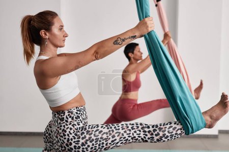 Retrato de vista lateral de mujer joven estirándose con hamaca y disfrutando de ejercicios de aero yoga, espacio para copiar