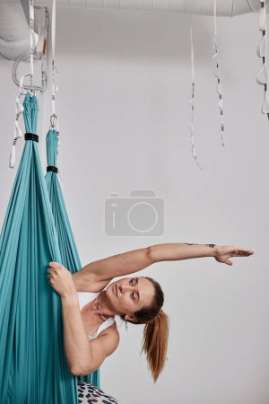 Vertical half portrait of young woman enjoying aero yoga in studio and stretching, copy space
