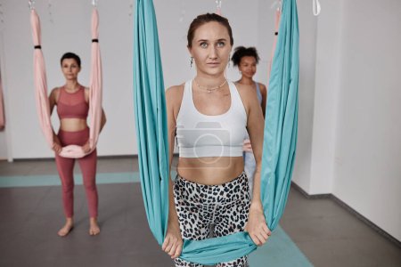 Diverso grupo de mujeres que están de pie junto a las hamacas en el estudio de yoga aéreo, espacio de copia