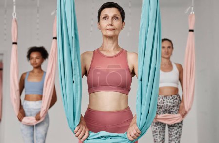 Waist up diverse group of women standing by hammocks in aero yoga studio