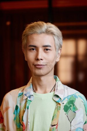 Vertikales Modeporträt eines jungen asiatischen Mannes mit gebleichten Haaren, der in die Kamera schaut