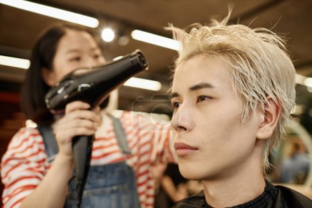 Nahaufnahme Porträt eines jungen asiatischen Mannes im Schönheitssalon mit Friseur, der die Haare trocknet, Kopierraum