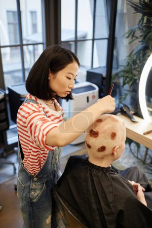Vertikale Seitenansicht Porträt der jungen Asiatin als Koloristin Malerei Haarkunst für weibliche Klientin im Schönheitssalon