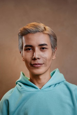 Vertikale Nahaufnahme Porträt eines jungen asiatischen Mannes mit gefärbten und gestylten Haaren, der im Studio in die Kamera schaut