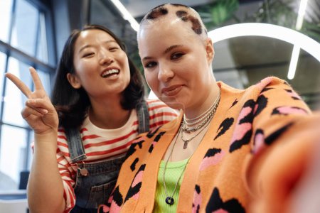 Téléchargez les photos : POV de souriante jeune femme aux cheveux créatifs prenant selfie dans un salon de beauté avec coiffeur - en image libre de droit