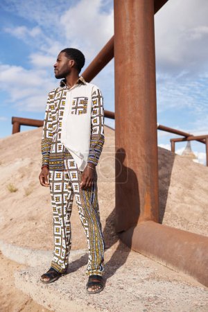 Full length fashion portrait of African American man wearing outfit with traditional pattern in desert sun