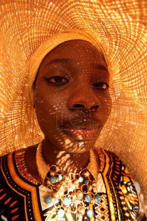 Fisheye portrait of young Black woman wearing traditional style clothing with straw hat shadow