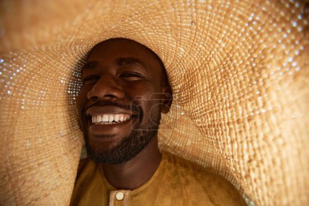Closeup of smiling Black man wearing giant straw hat laughing happily outdoors, copy space