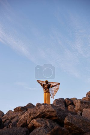 Retrato de gran angular de una joven negra de pie en la cima de la montaña y bailando con velo, espacio para copiar