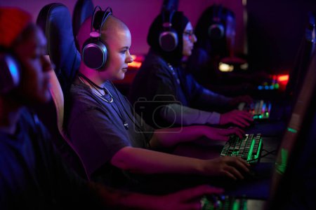 Photo for Side view portrait of gen Z young woman playing video games in cybersports club with group of people in row, copy space - Royalty Free Image