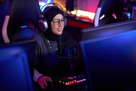 Photo for High angle portrait of Muslim young woman playing video games in cybersports club and wearing pro headphones, copy space - Royalty Free Image