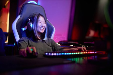 Photo for Portrait of smiling Asian woman enjoying video games in cybersports club with neon lights, copy space - Royalty Free Image
