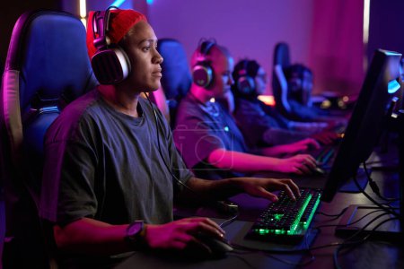 Photo for Side view portrait of Black woman playing video games professionally in cybersports club with neon lighting, copy space - Royalty Free Image