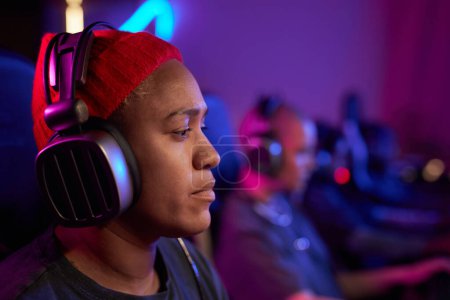 Photo for Side view closeup of African American woman playing video games in cybersports club and wearing pro headphones, copy space - Royalty Free Image