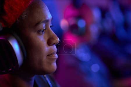 Photo for Close up profile view of smiling Black woman playing video games professionally in neon lighting and wearing headphones, copy space - Royalty Free Image