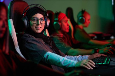 Photo for Portrait of Muslim young woman playing video games and looking at camera in pro cybersports team, copy space - Royalty Free Image