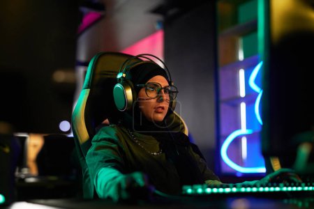 Photo for Portrait of Muslim young woman playing videogames in neon light and wearing headphones, cyberpunk style - Royalty Free Image