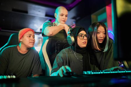 Photo for Portrait of Muslim young woman playing video game in cybersports club with diverse team of young women cheering - Royalty Free Image