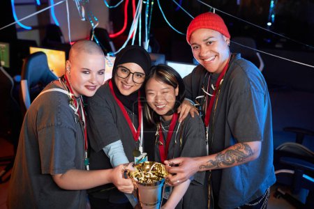 Photo for Diverse team of professional female gamers celebrating victory in eSports championship and holding golden cup - Royalty Free Image