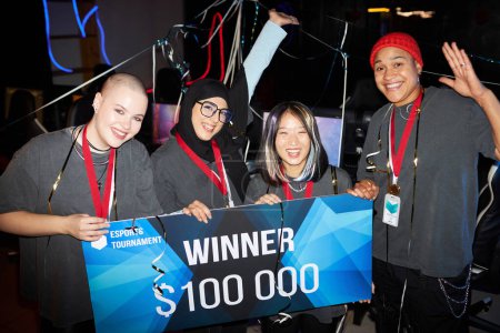 Photo for Diverse team of professional female gamers celebrating victory in eSports championship and holding big cash check - Royalty Free Image