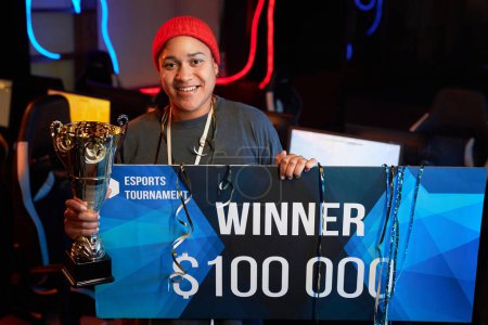 Photo for Waist up portrait of African American woman holding golden cup and prize money check after winning eSports tournament, copy space - Royalty Free Image