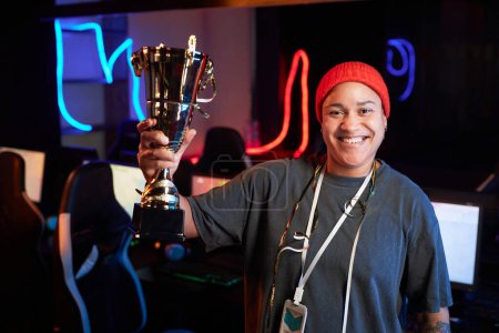 Photo for Waist up portrait of smiling Black woman holding golden cup and smiling at camera celebrating victory in eSports tournament, copy space - Royalty Free Image