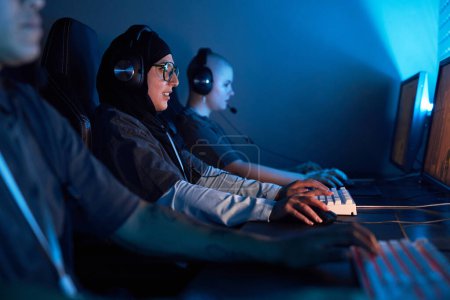 Photo for Side view portrait of Muslim young woman playing video games in blue neon light, copy space - Royalty Free Image