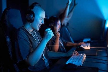 Photo for Portrait of happy young woman playing video games and celebrating victory in blue light - Royalty Free Image