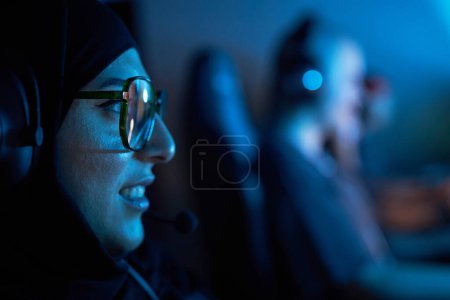 Photo for Side view closeup of Arab young woman playing video games in blue neon light, copy space - Royalty Free Image