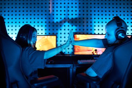 Photo for Back view of two young women playing video games and celebrating victory in blue light - Royalty Free Image